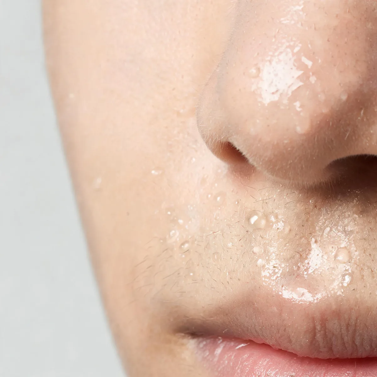 Skin of the upper lip and side of the nose showing fine sweat droplets and an oily sheen, no facial identity and no eyes.